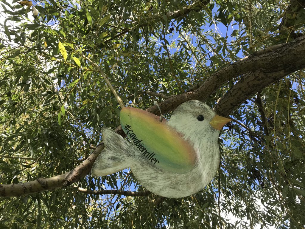 Un oiseau de bois dont les ailes sont aux couleurs de l'arc-en-ciel